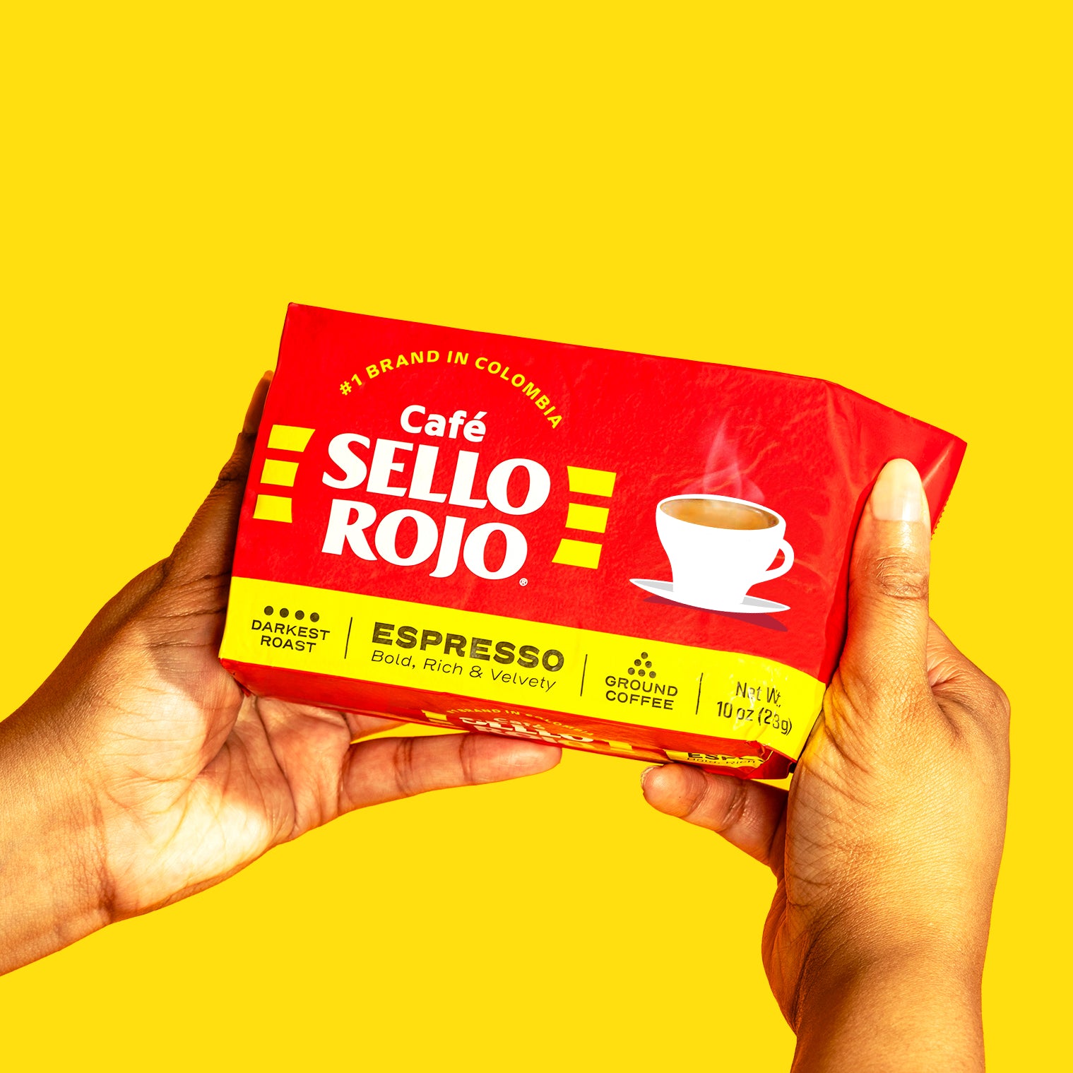 Café Sello Rojo espresso coffee package held by a hand against a yellow background